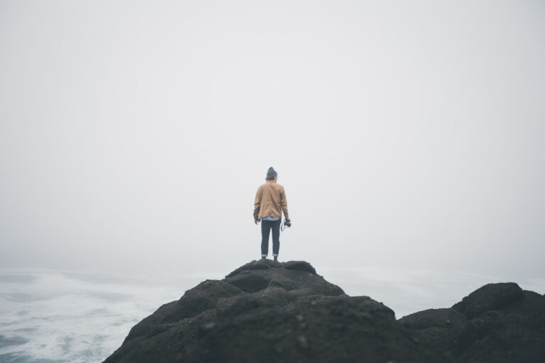 A man stands on a rocky mountain under a white sky